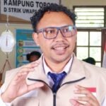 Seorang pejabat berbicara di posyandu di depan ibu-ibu dan balita, dengan timbangan bayi (dacin) dan poster Posyandu Kampung Topo di latar