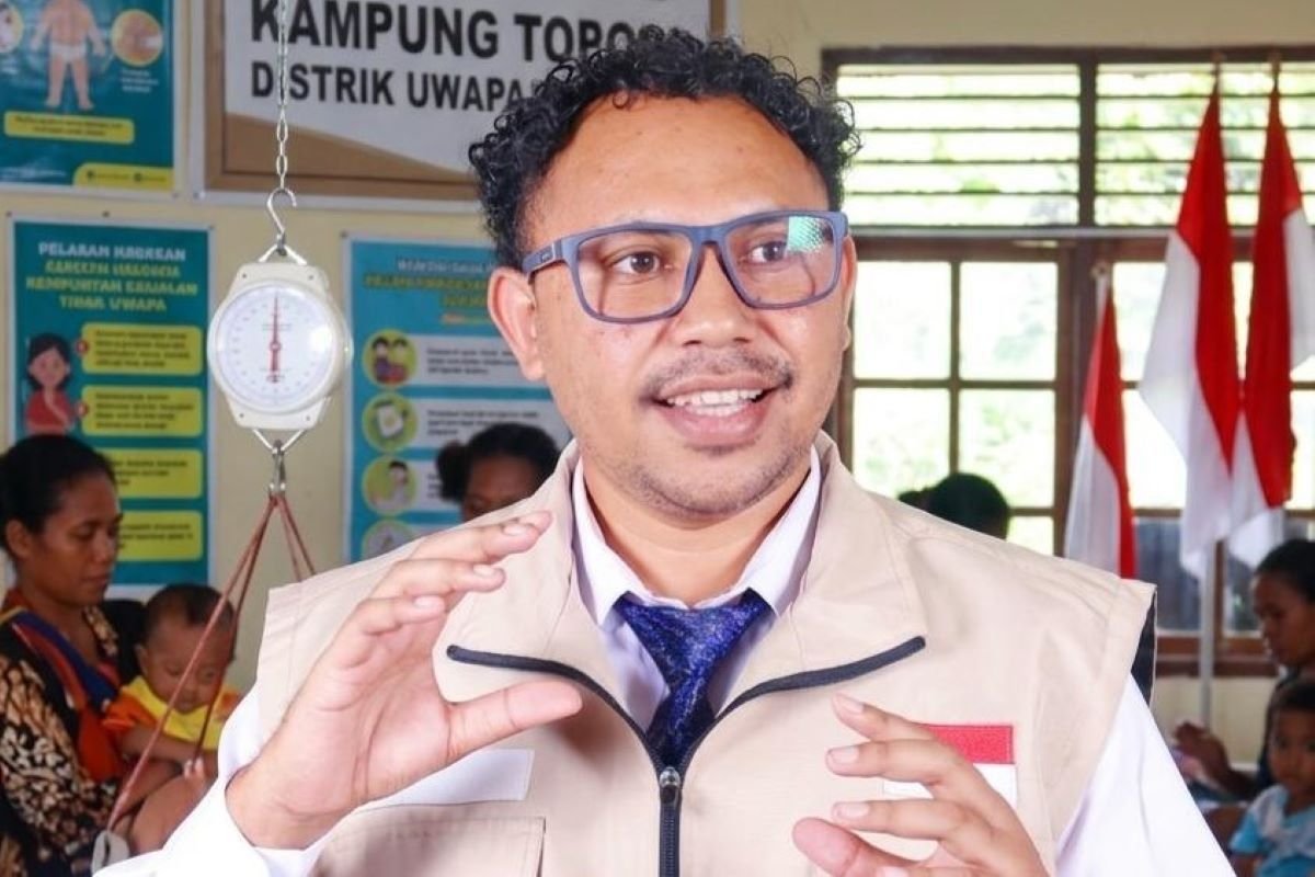 Seorang pejabat berbicara di posyandu di depan ibu-ibu dan balita, dengan timbangan bayi (dacin) dan poster Posyandu Kampung Topo di latar