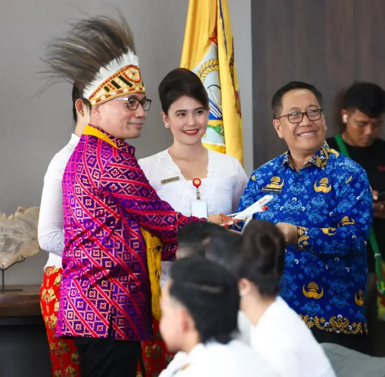 Penyambutan penerbangan perdana di Nabire: penari berpakaian adat Papua dan awak maskapai dalam acara penyerahan, dengan Bendera Papua Tengah di latar