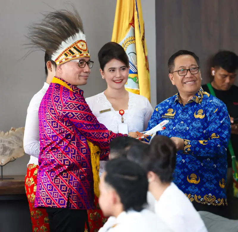 Penyambutan penerbangan perdana di Nabire: penari berpakaian adat Papua dan awak maskapai dalam acara penyerahan, dengan Bendera Papua Tengah di latar