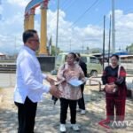 Beberapa orang berdiri di pelataran Taman Gizi Nabire dengan pilar dan kendaraan di latar, memperlihatkan suasana relokasi pedagang.
