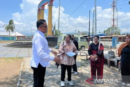 Beberapa orang berdiri di pelataran Taman Gizi Nabire dengan pilar dan kendaraan di latar, memperlihatkan suasana relokasi pedagang.