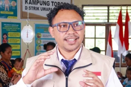 Seorang pejabat berbicara di posyandu di depan ibu-ibu dan balita, dengan timbangan bayi (dacin) dan poster Posyandu Kampung Topo di latar