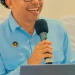 Seorang pria berbaju biru memegang mikrofon saat berbicara