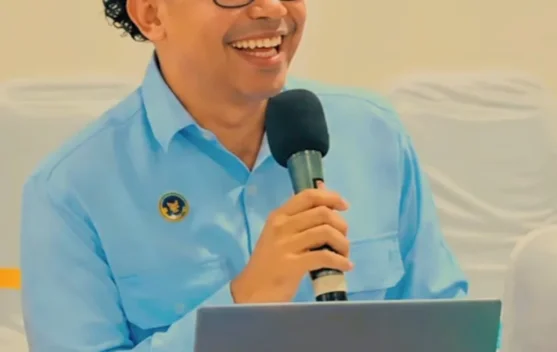 Seorang pria berbaju biru memegang mikrofon saat berbicara