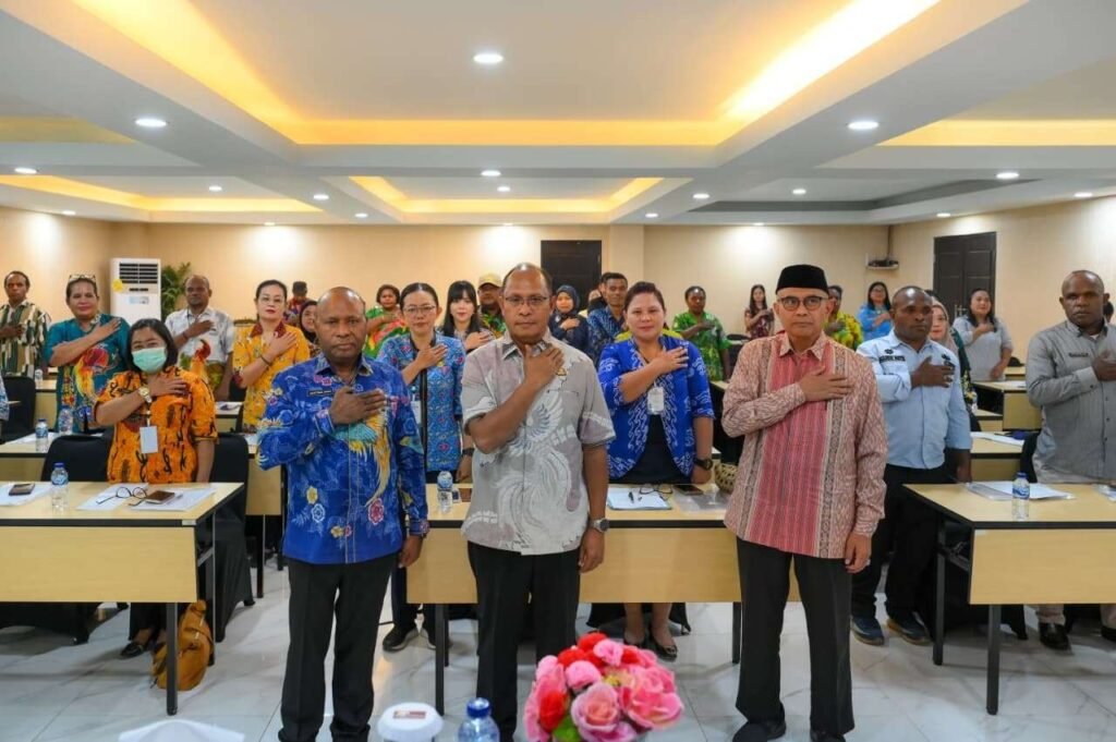 Peserta dan pejabat berdiri dengan tangan di dada di ruang pelatihan