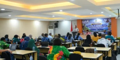 Peserta duduk menghadap pembicara di podium dengan spanduk Training of Trainers di ruang pertemuan