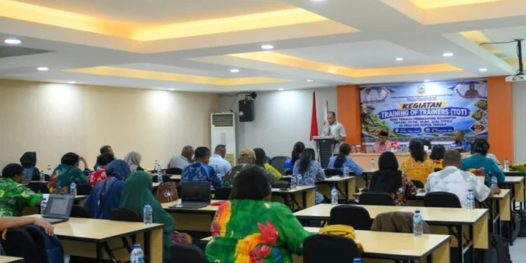 Peserta duduk menghadap pembicara di podium dengan spanduk Training of Trainers di ruang pertemuan